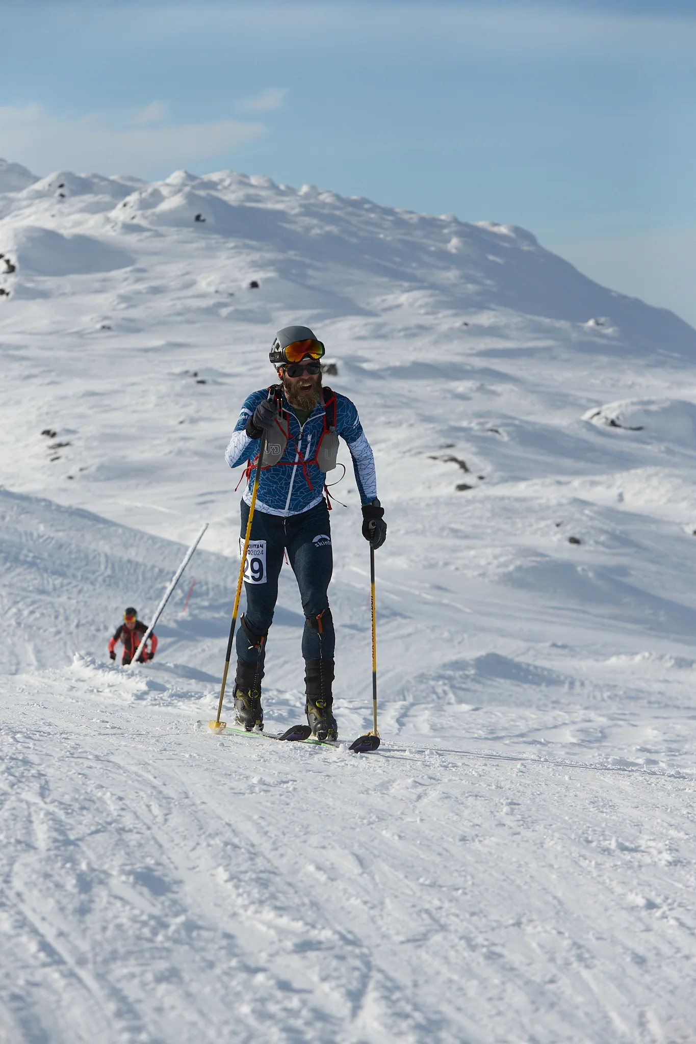 En skidalpinist på väg upp längs en snötäckt fjällrygg med vida fjäll i bakgrunden