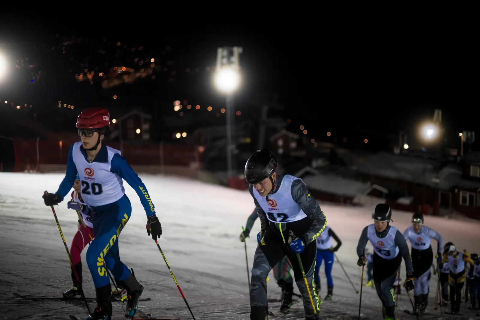 Skidalpinister klättrar i en upplyst skidbacke under Åres mörka natthimmel